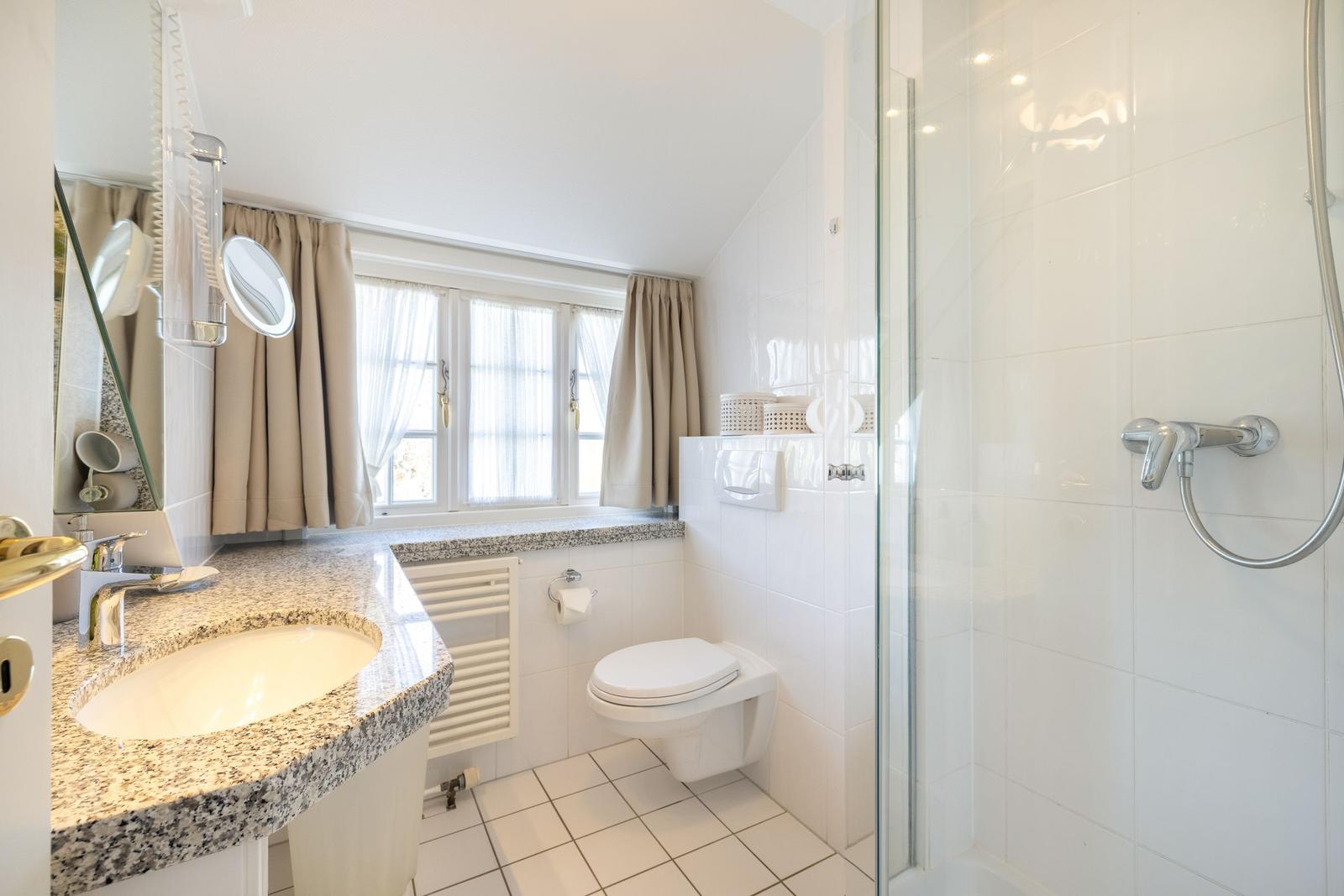 Bad mit Dusche, Waschbecken und Toilette. Fenster mit Vorhängen.