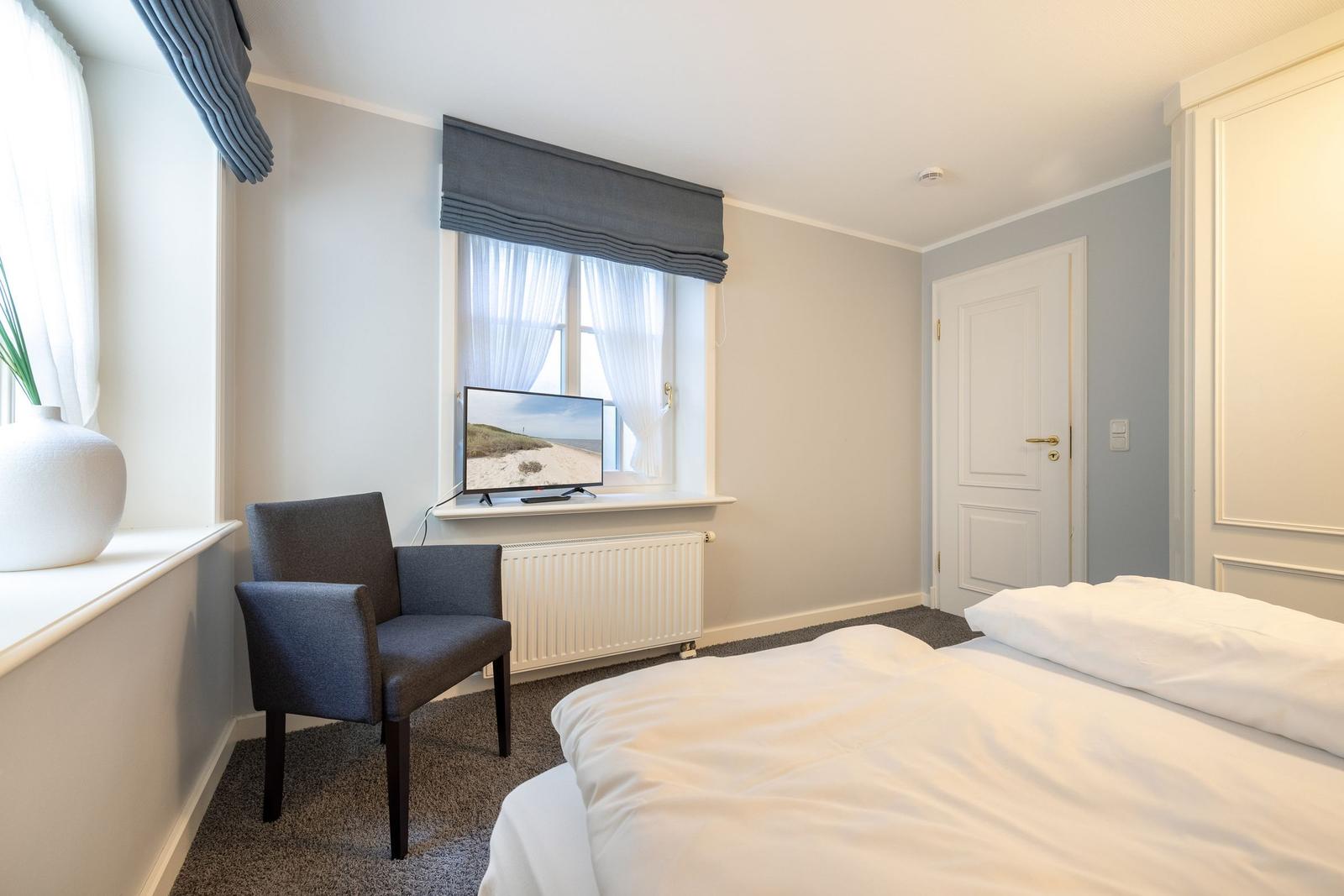 Ein Schlafzimmer mit Bett, Stuhl und TV vor dem Fenster.