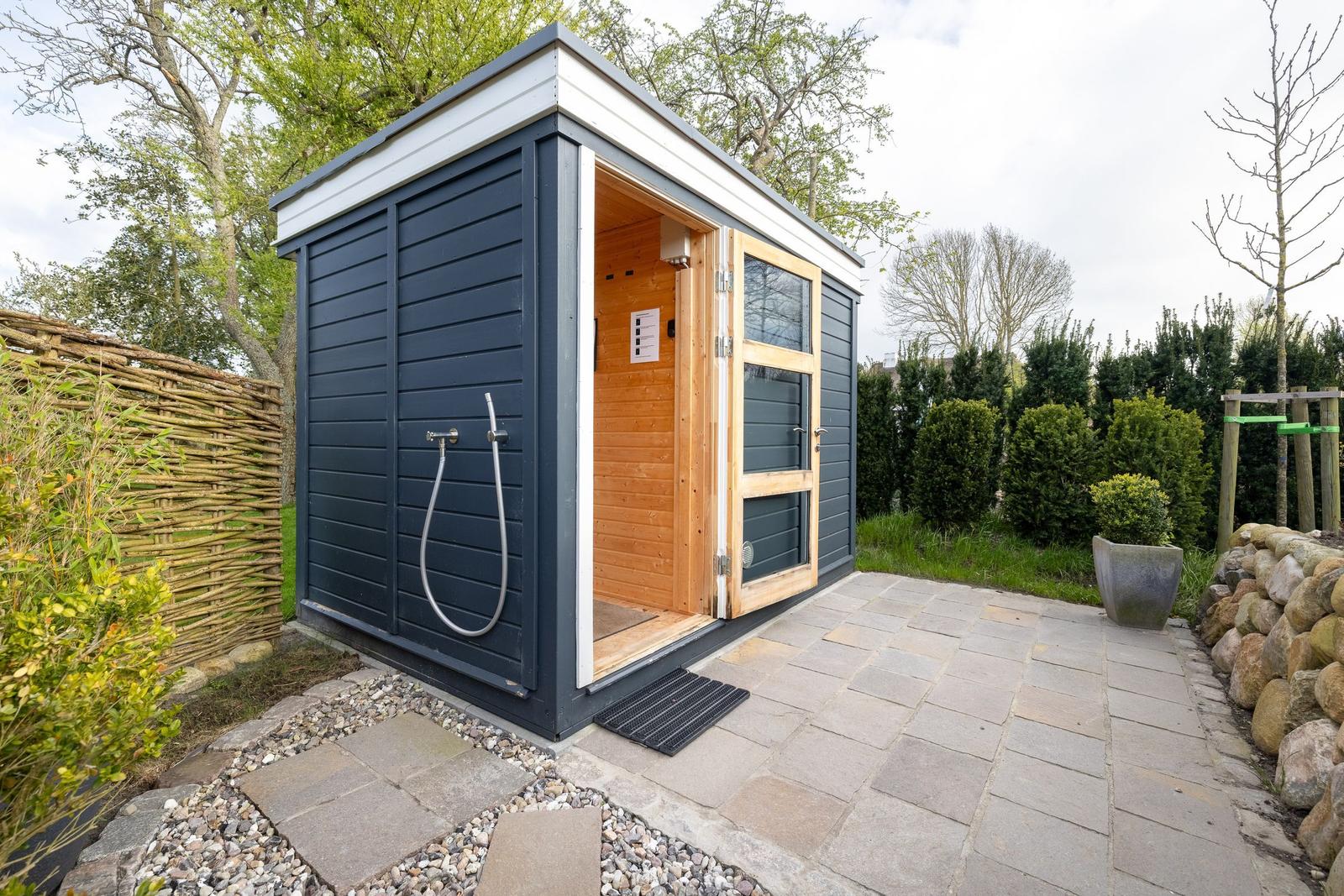 Außenliegende Sauna mit Holztür und Duschvorrichtung im Garten.