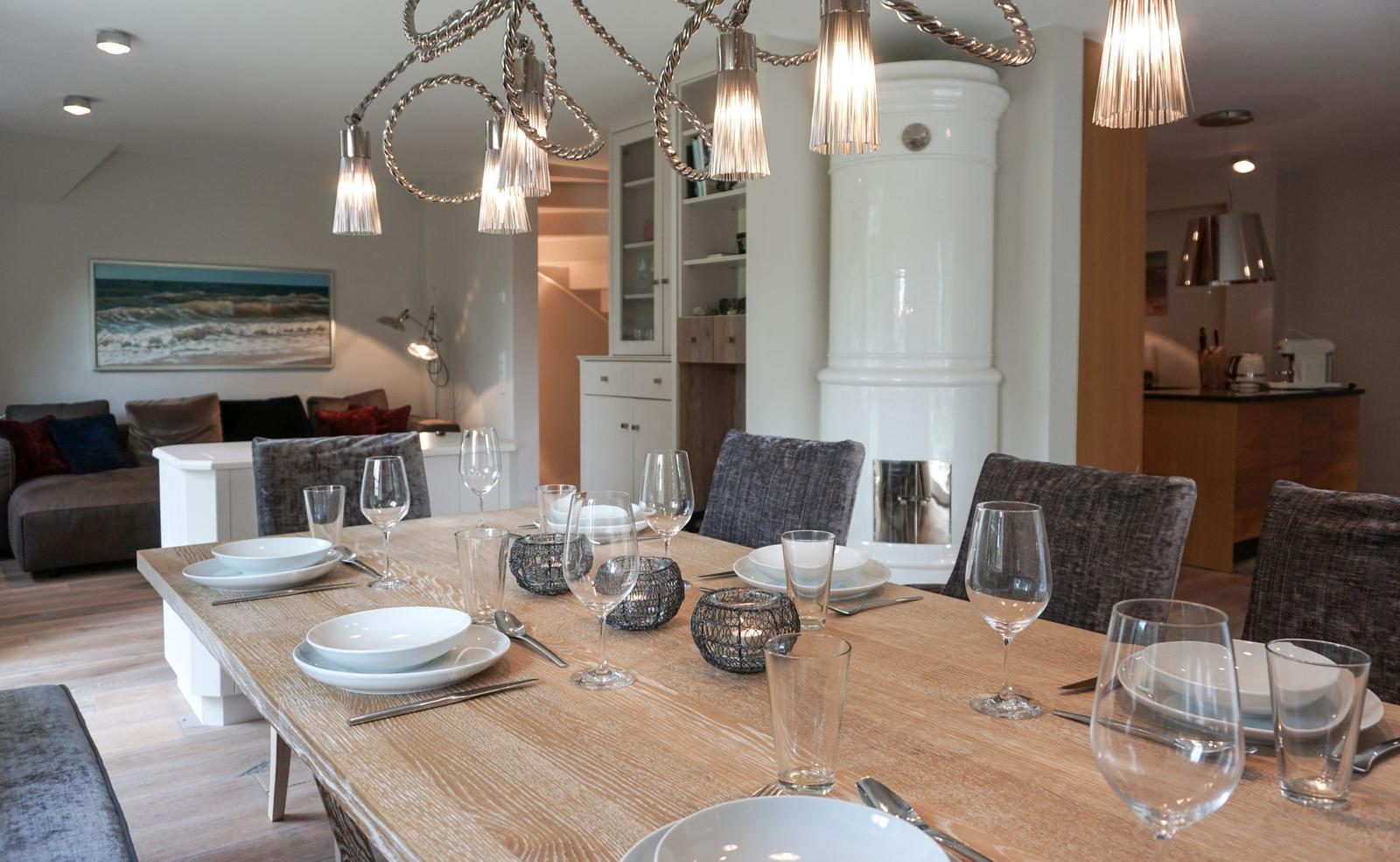 Dining area with wooden table, chairs, and pendant lights. Living room and kitchen in background.