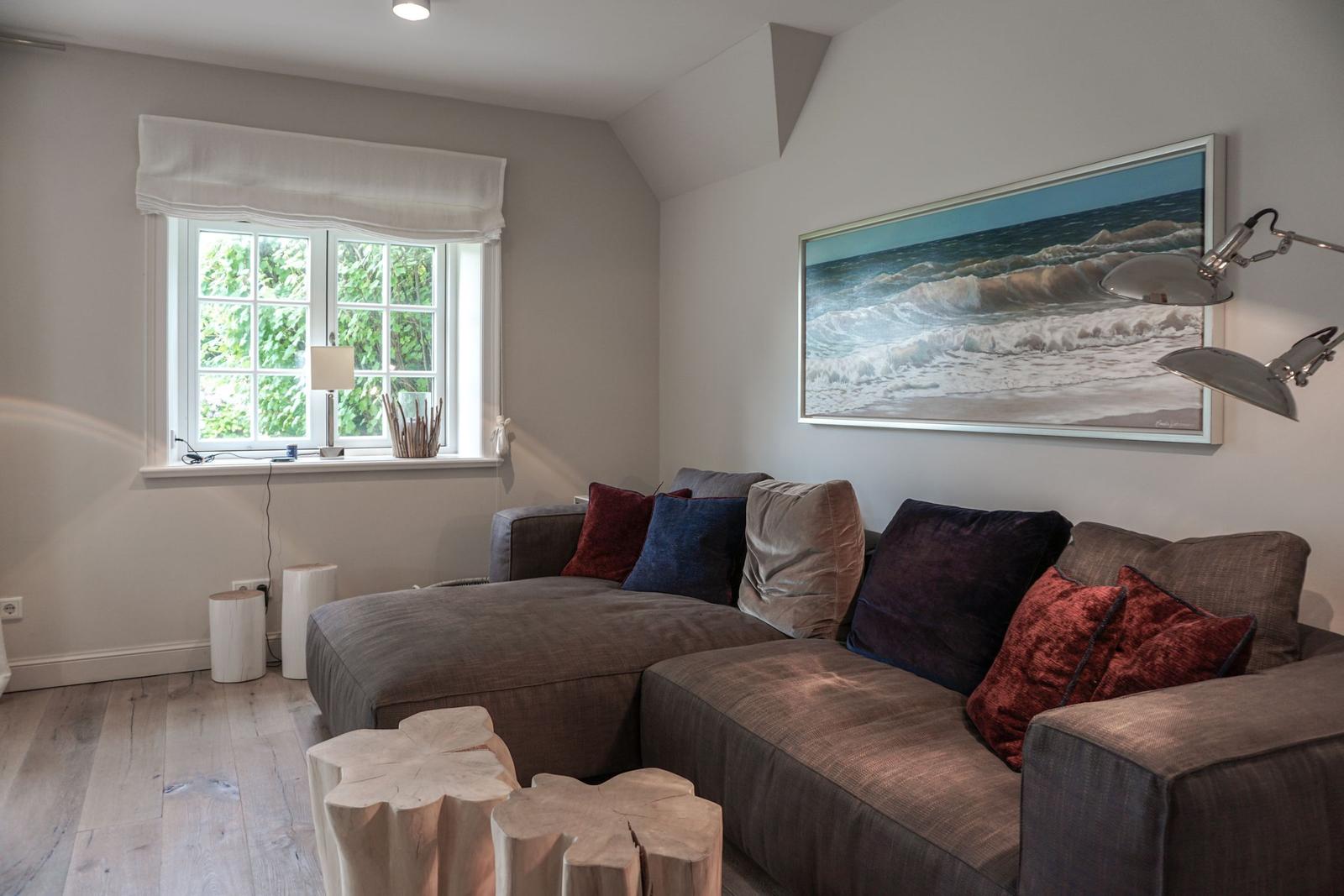 A living room with a gray sofa, a window, and a wall painting.