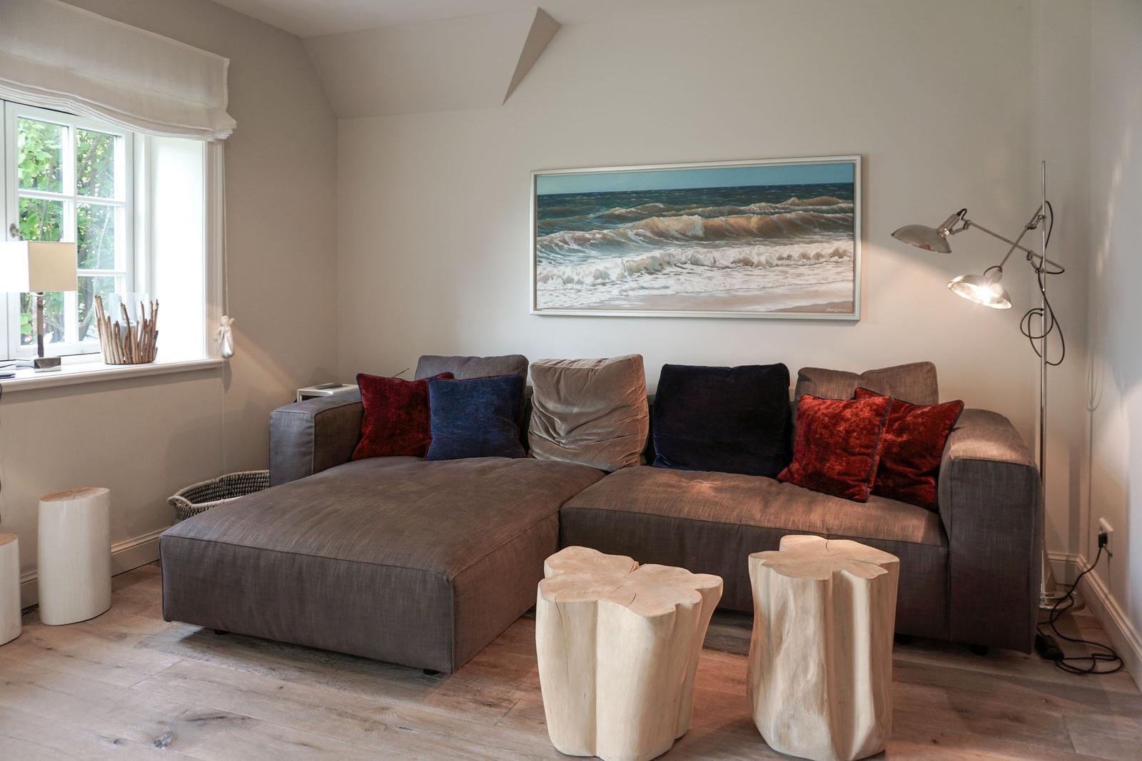 A living room with gray sofa, red and blue cushions, wooden tables, and wall art.