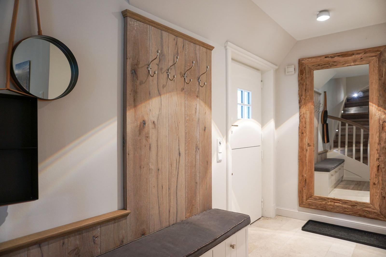 Entrance with wooden wall, hooks, and mirror. Staircase visible in the background.