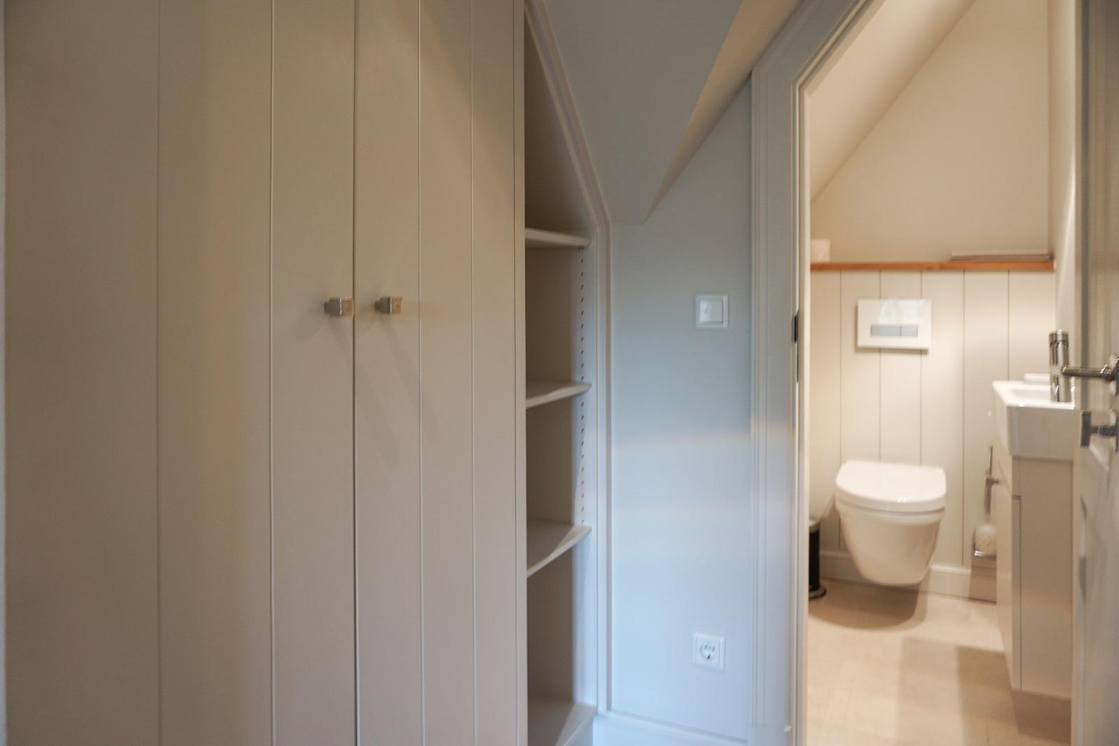 Bedroom with wardrobe and view into bathroom with toilet and sink.