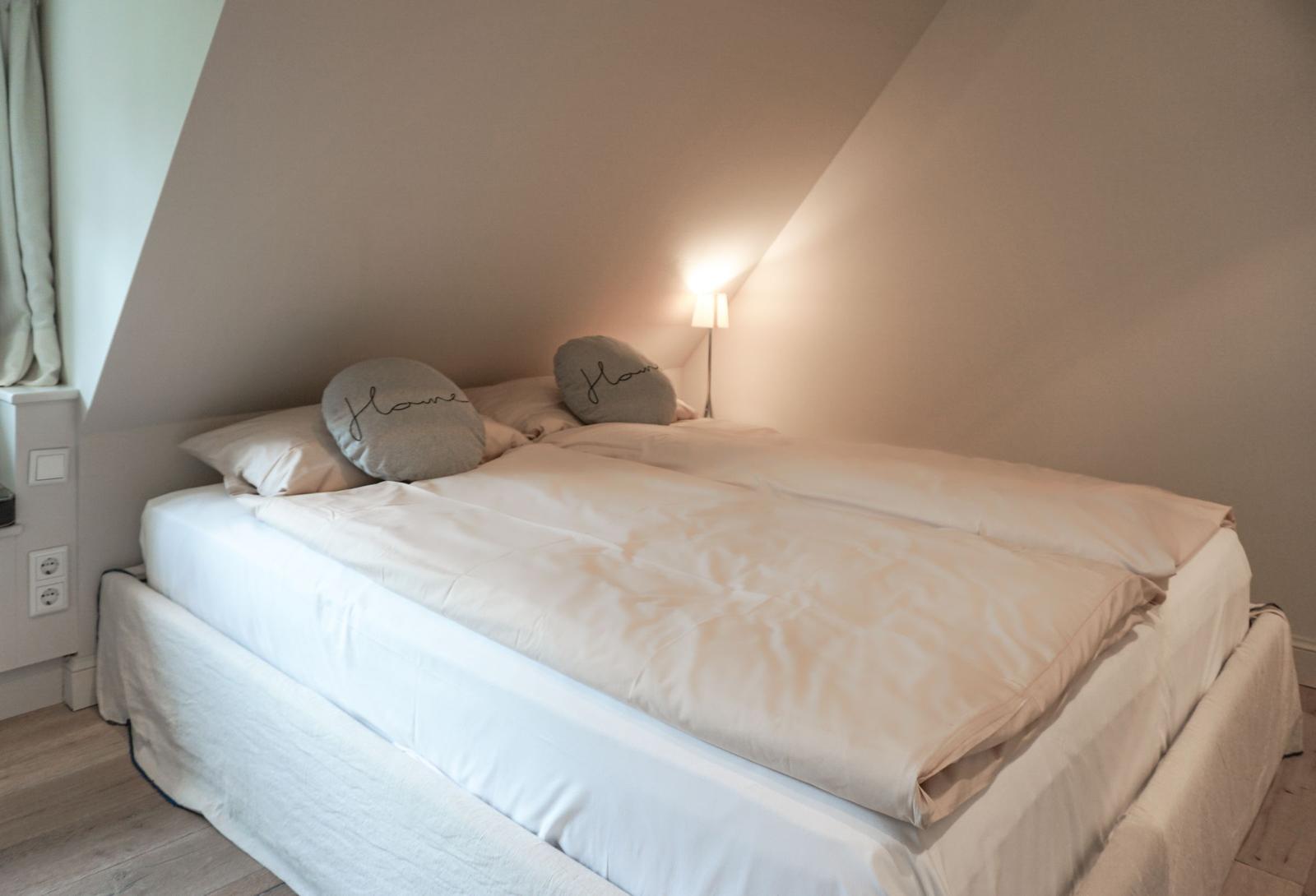 Bedroom with double bed, two pillows with text, and standing lamp.