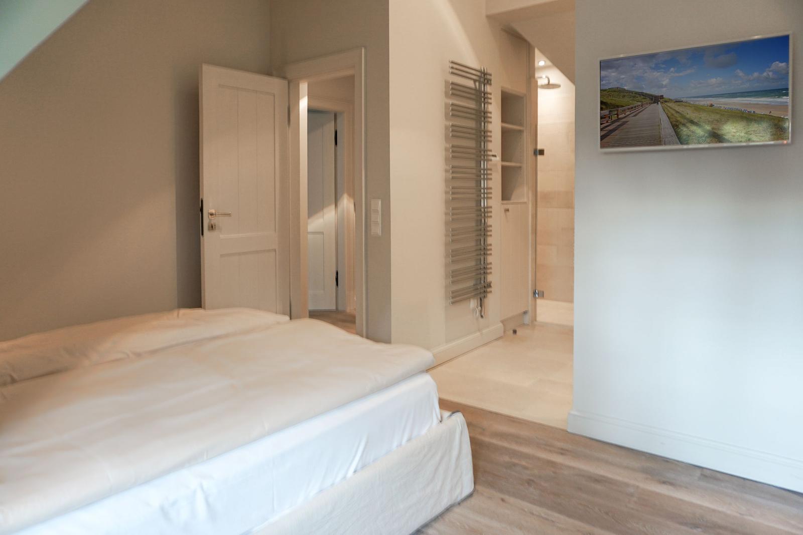 Bedroom with bed, door, and bathroom. Wall picture shows beach.
