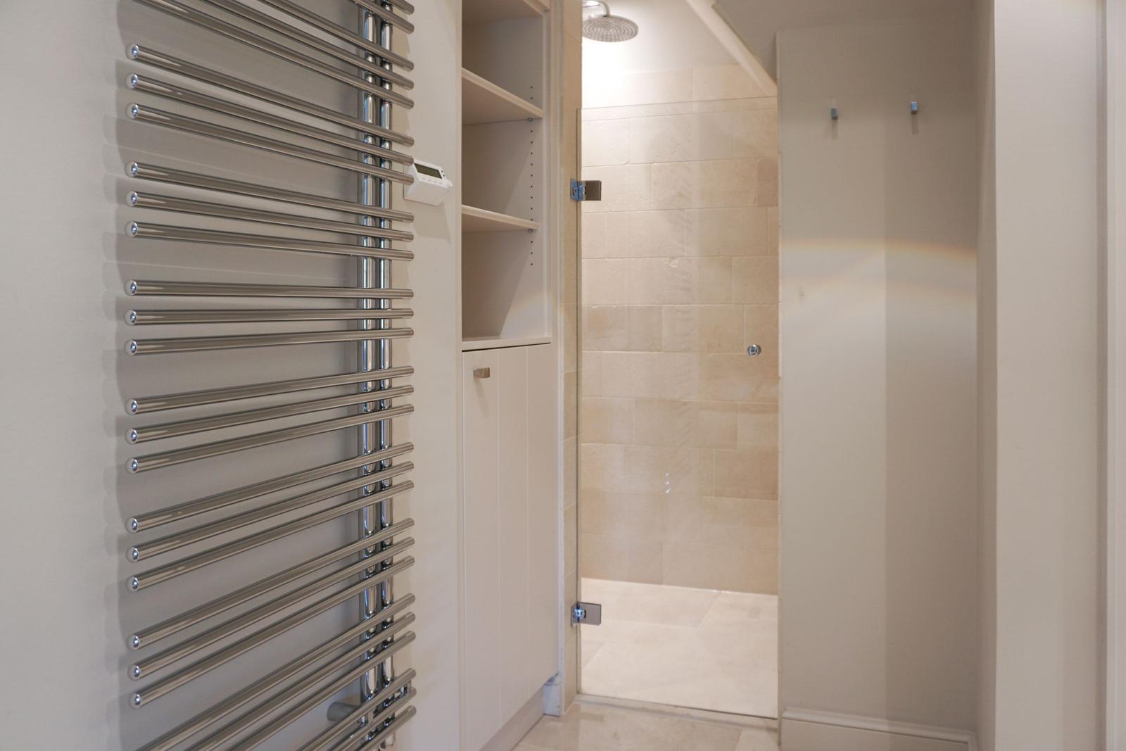 Shower with stone tiles and heater on the wall.