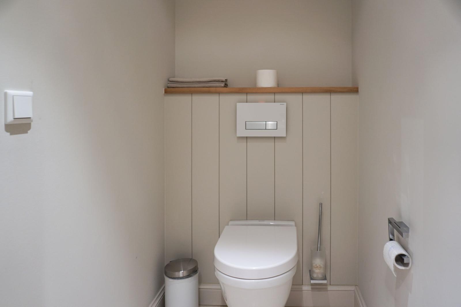 Toilet with wooden shelf, toilet paper, and brush holder