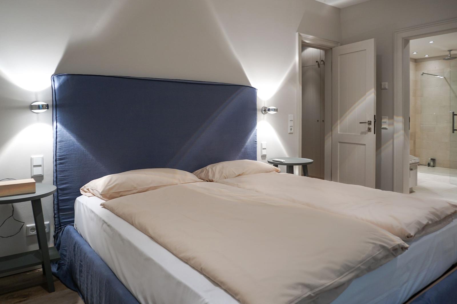 Bedroom with double bed, blue headboard, and nightstands. View into the bathroom.