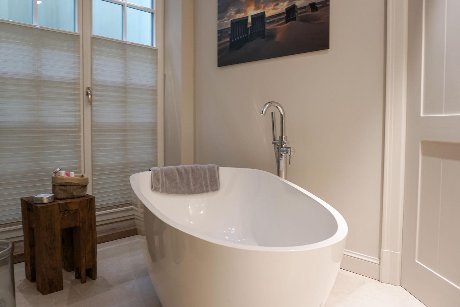 Freestanding bathtub with shower faucet and window with blinds.