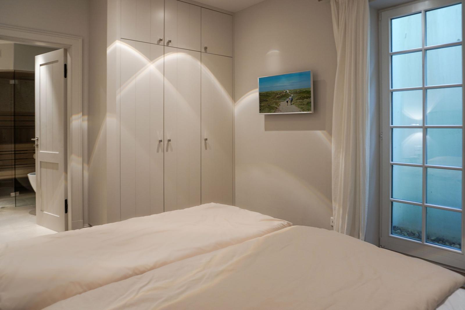 Bedroom with bed, wardrobe, and window. Passage to sauna visible.
