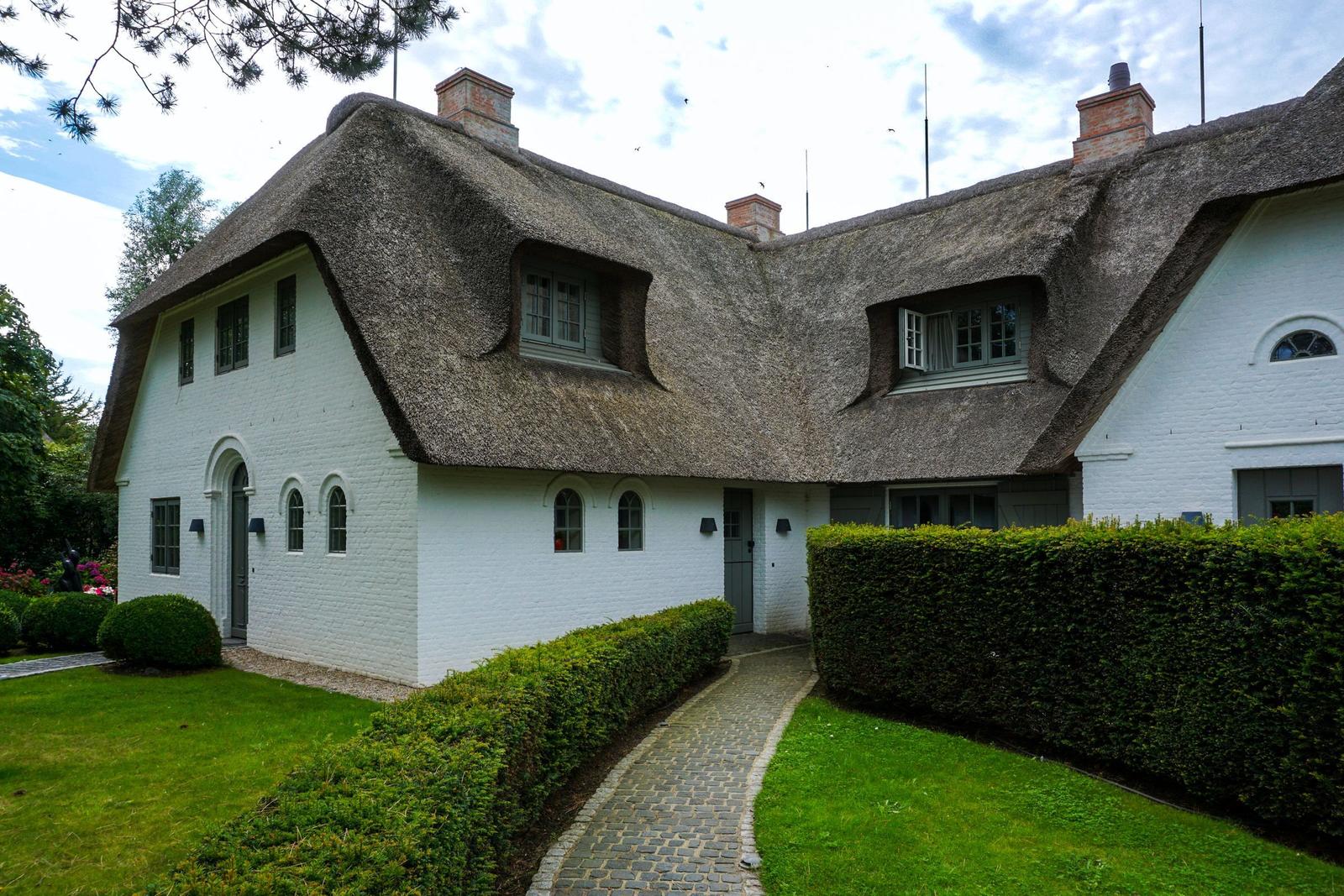 White house with thatched roof and manicured garden.