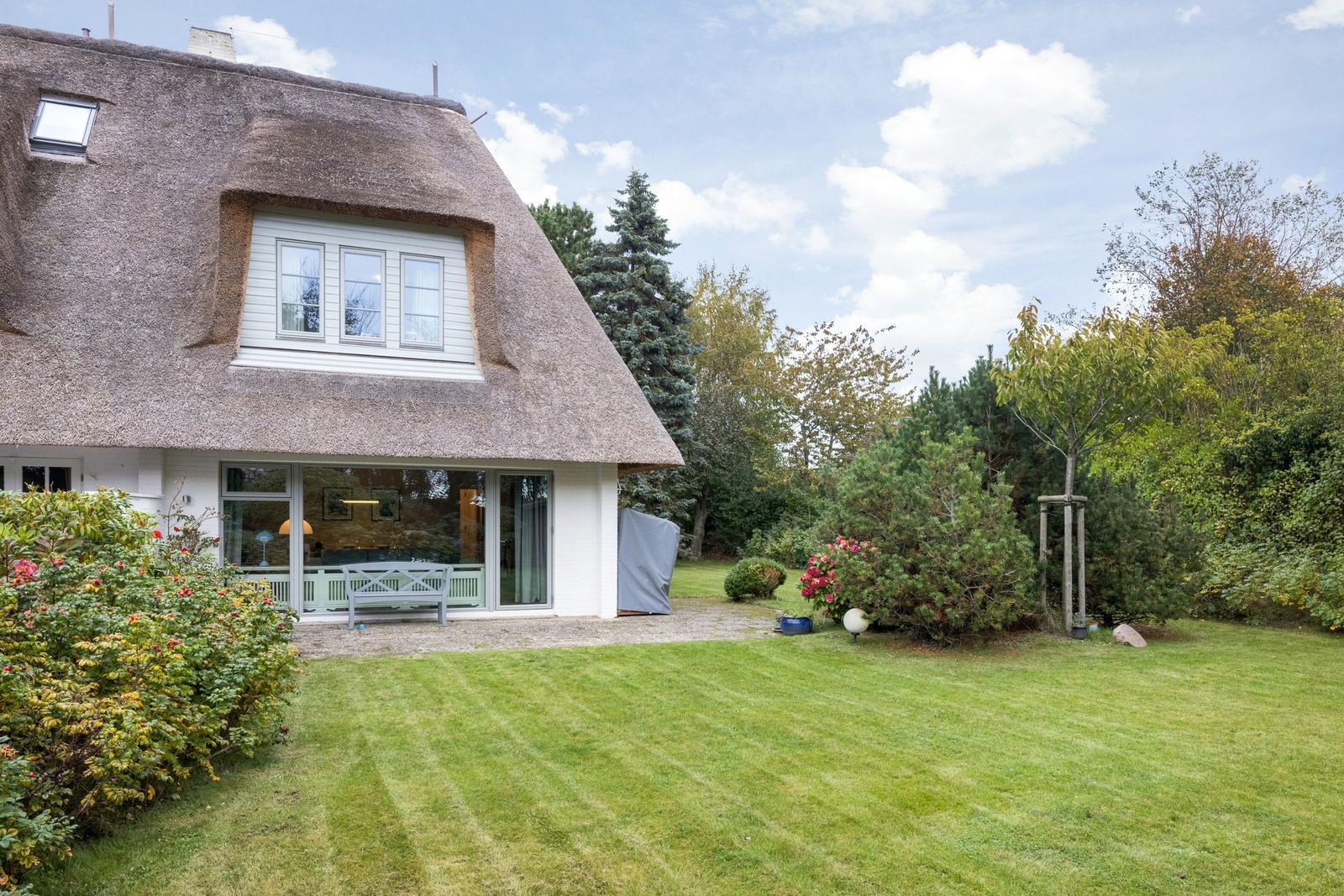 Haus mit Strohdach, großem Garten und Glasfront zur Terrasse.