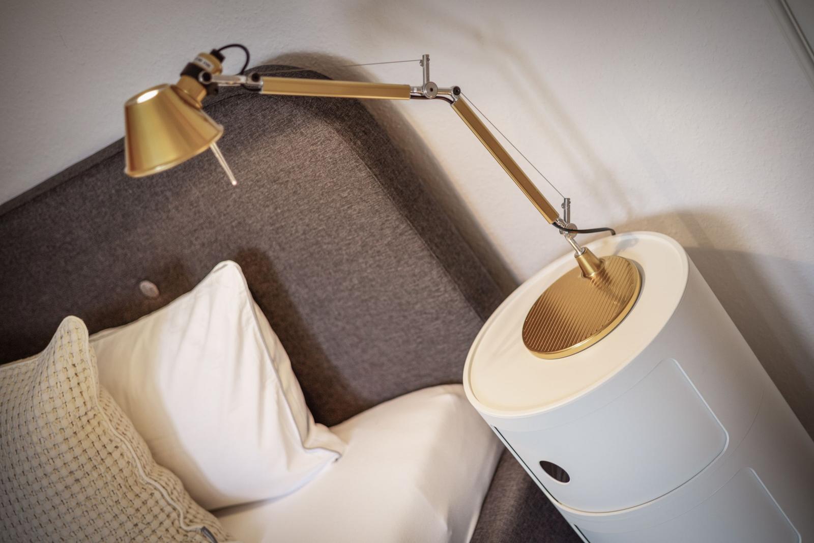Graue Couch mit weißen Kissen und goldener Stehlampe auf weißem Beistelltisch.