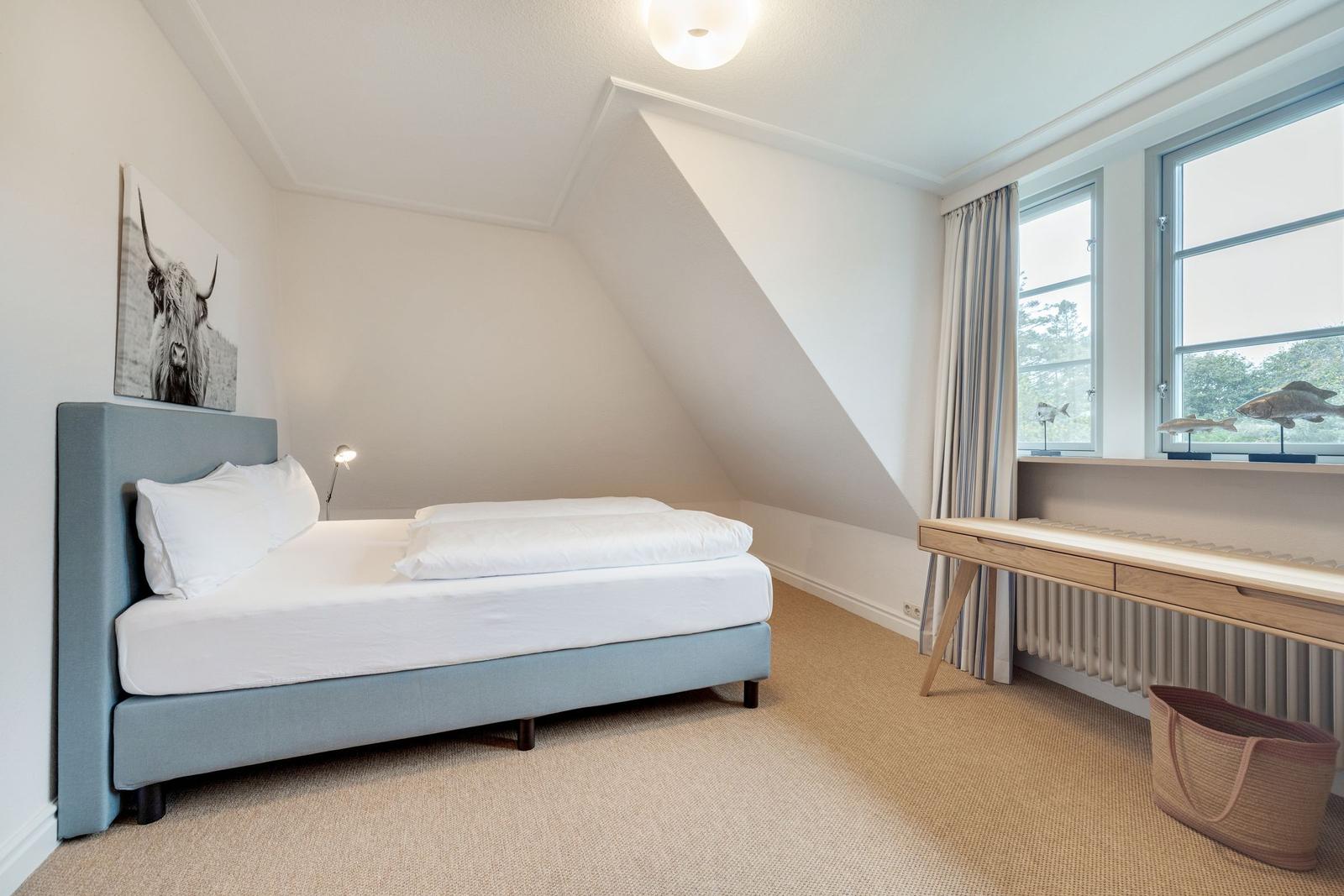 Schlafzimmer mit Dachschräge, Bett, Schreibtisch und Fenster.