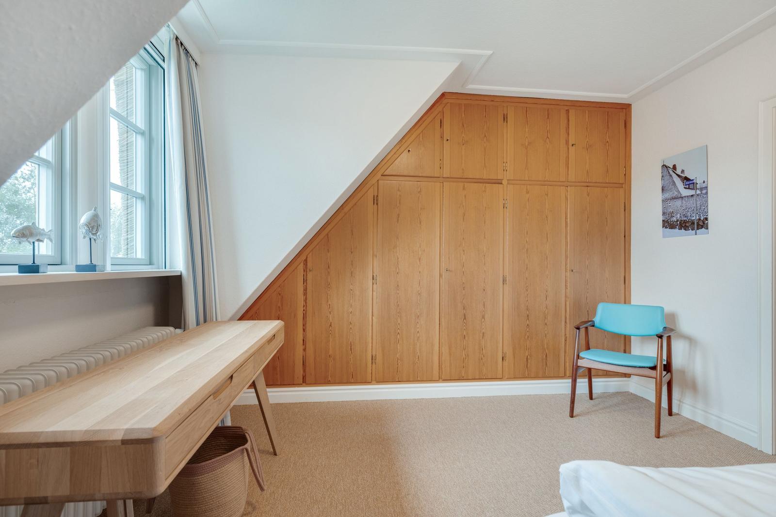 Schlafzimmer mit Holzschrank, Schreibtisch und blauer Sitzgelegenheit.
