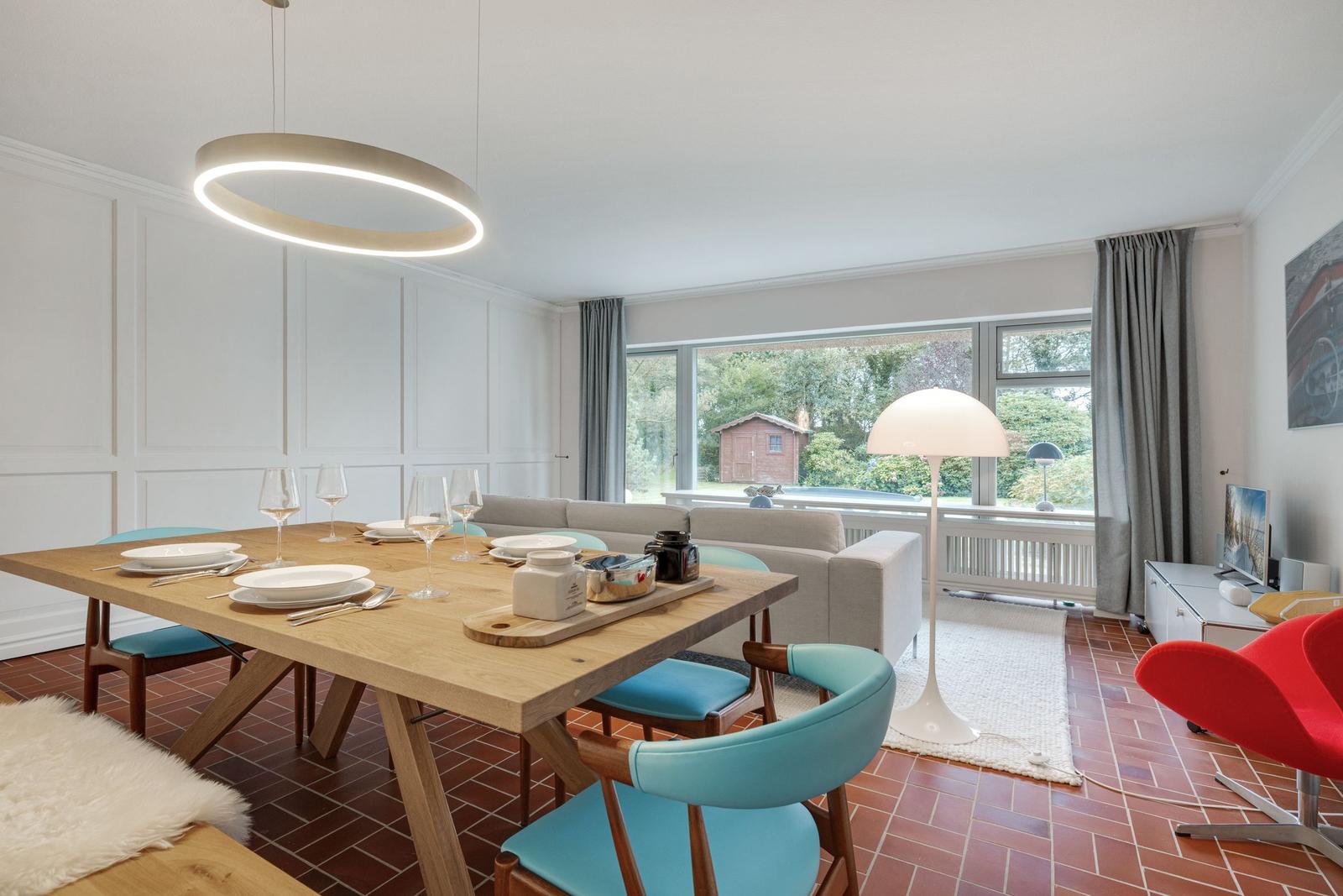 Esszimmer mit Holztisch, blauen Stühlen und großem Fenster zur Gartenansicht.