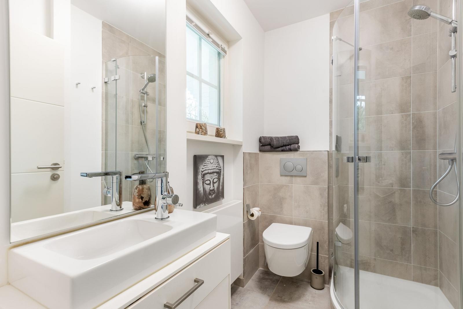 Bathroom with shower, sink, and toilet. Window and Buddha picture visible.
