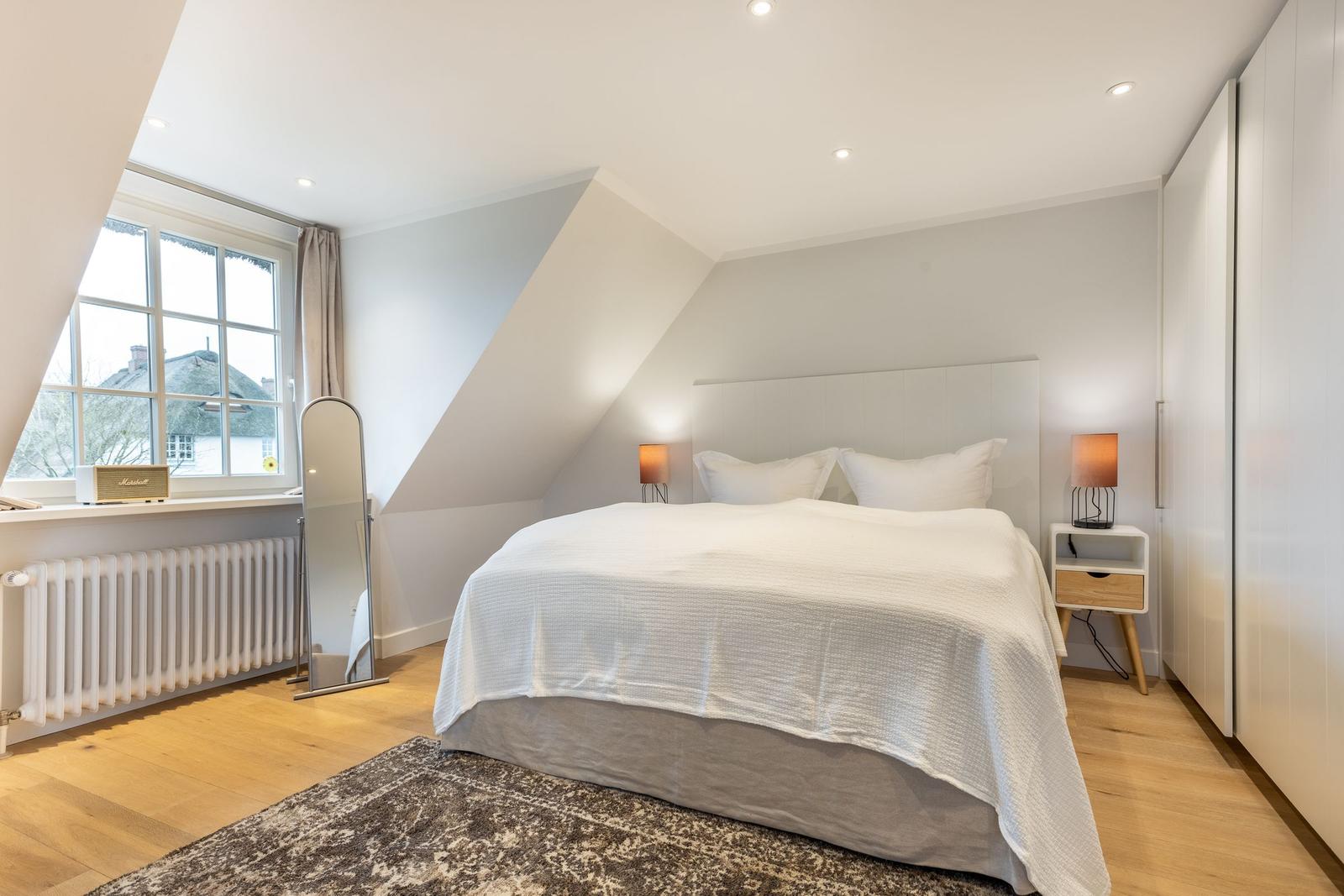Bedroom with sloped ceiling, bed, nightstand, and window.
