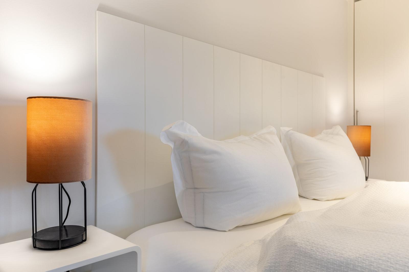 Bedroom with white bed, headboard, and nightstand with lamp.