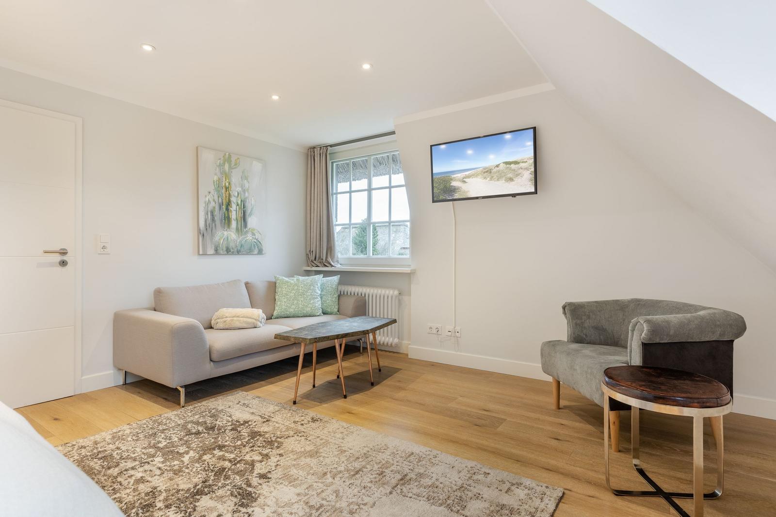 Living room with sofa, armchair, TV, and wooden floor.