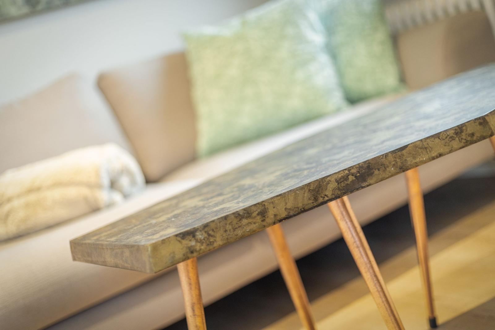 A table with wooden legs and a metallic-looking top in front of a sofa.