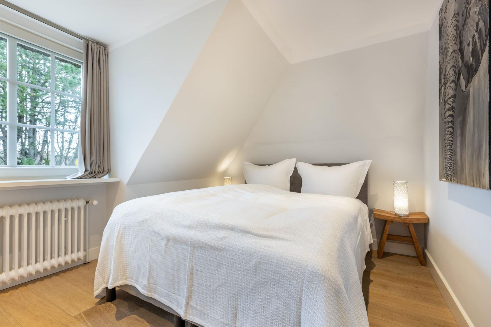 Bedroom with sloped ceiling, window, and bed with white pillows.