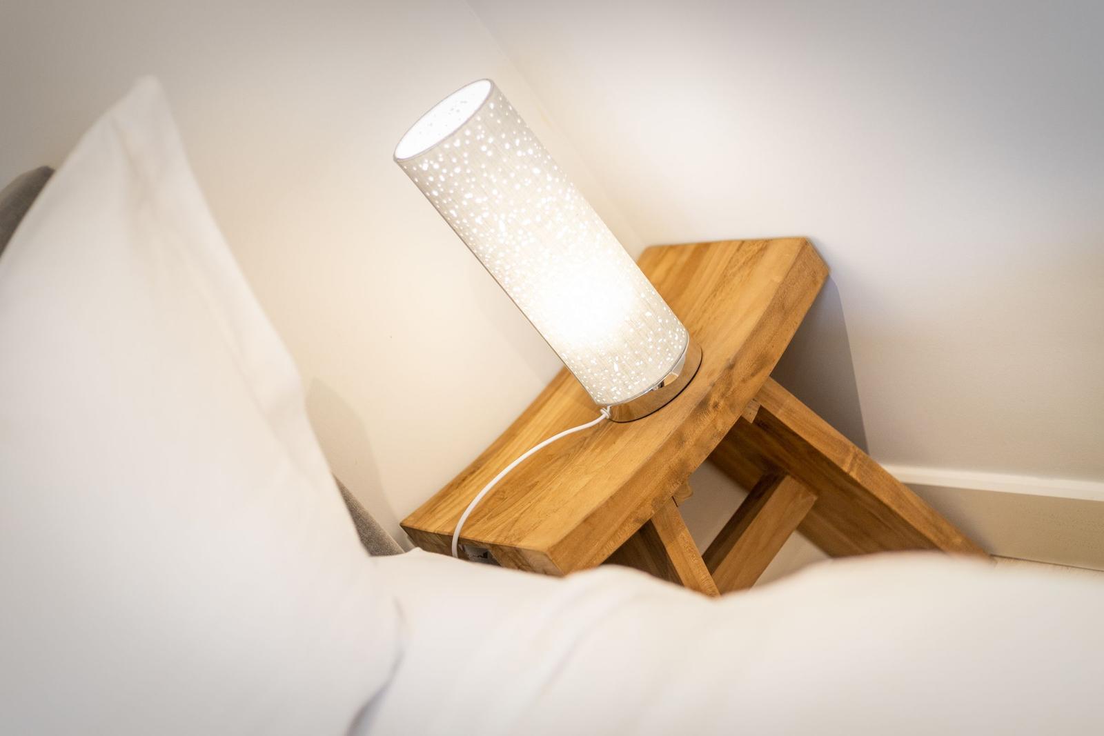 A lamp on a wooden table next to a bed