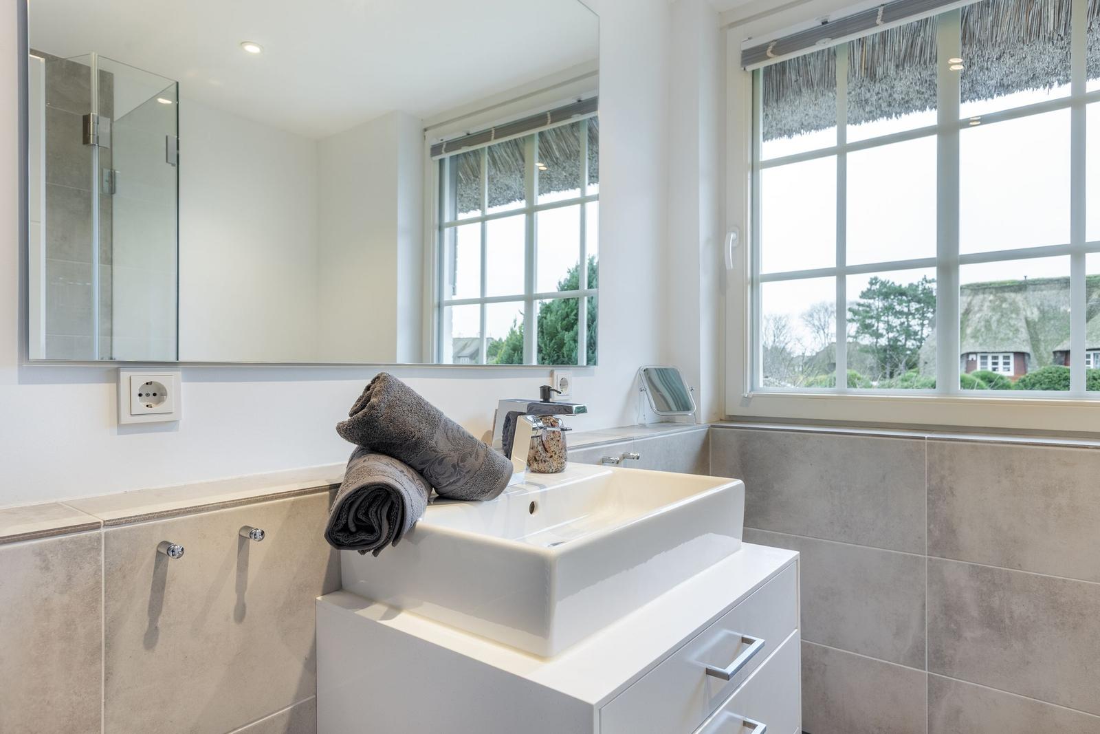 Bathroom with sink, mirror, and window with thatched roof view.