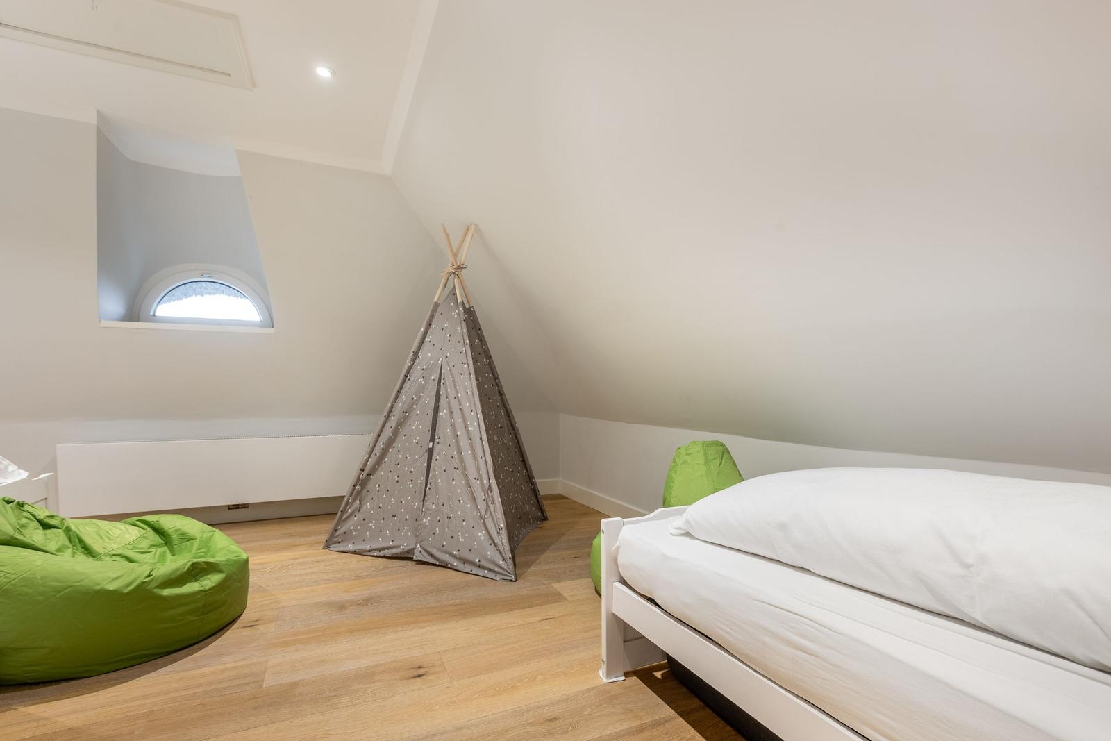 Bedroom with sloped ceiling, bed, teepee, and green bean bags.