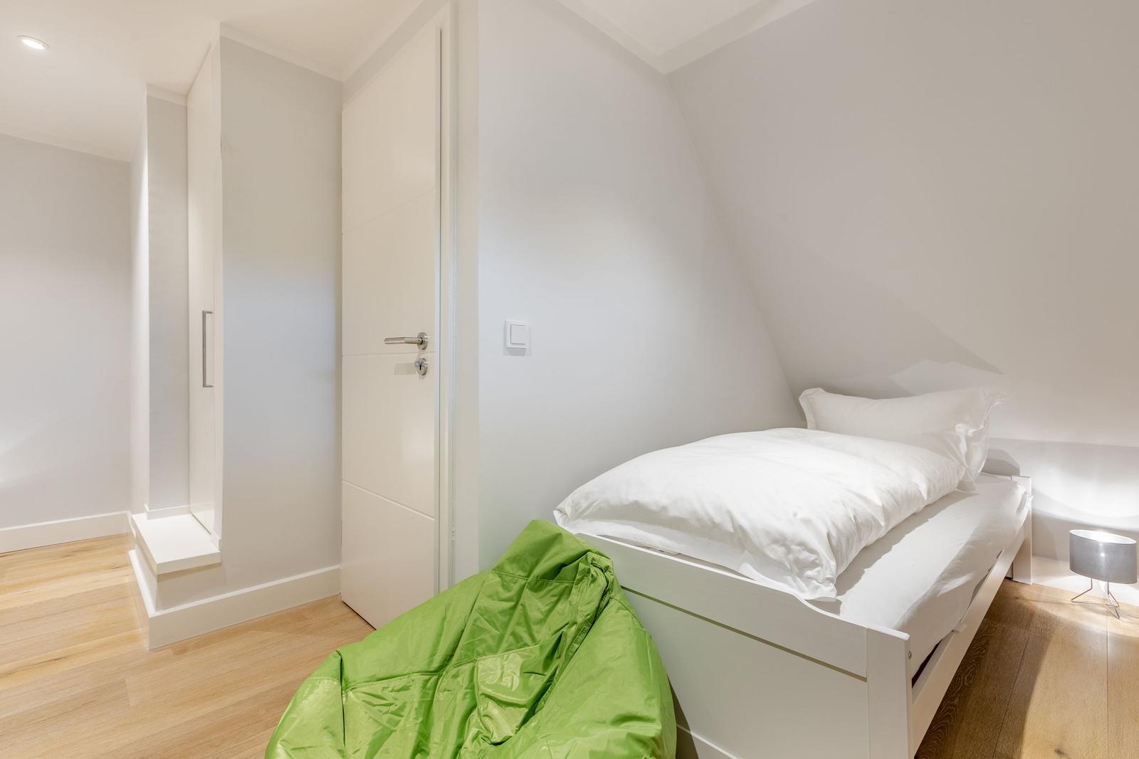 Bedroom with sloped ceiling, white bed, and green bean bag on wooden floor.