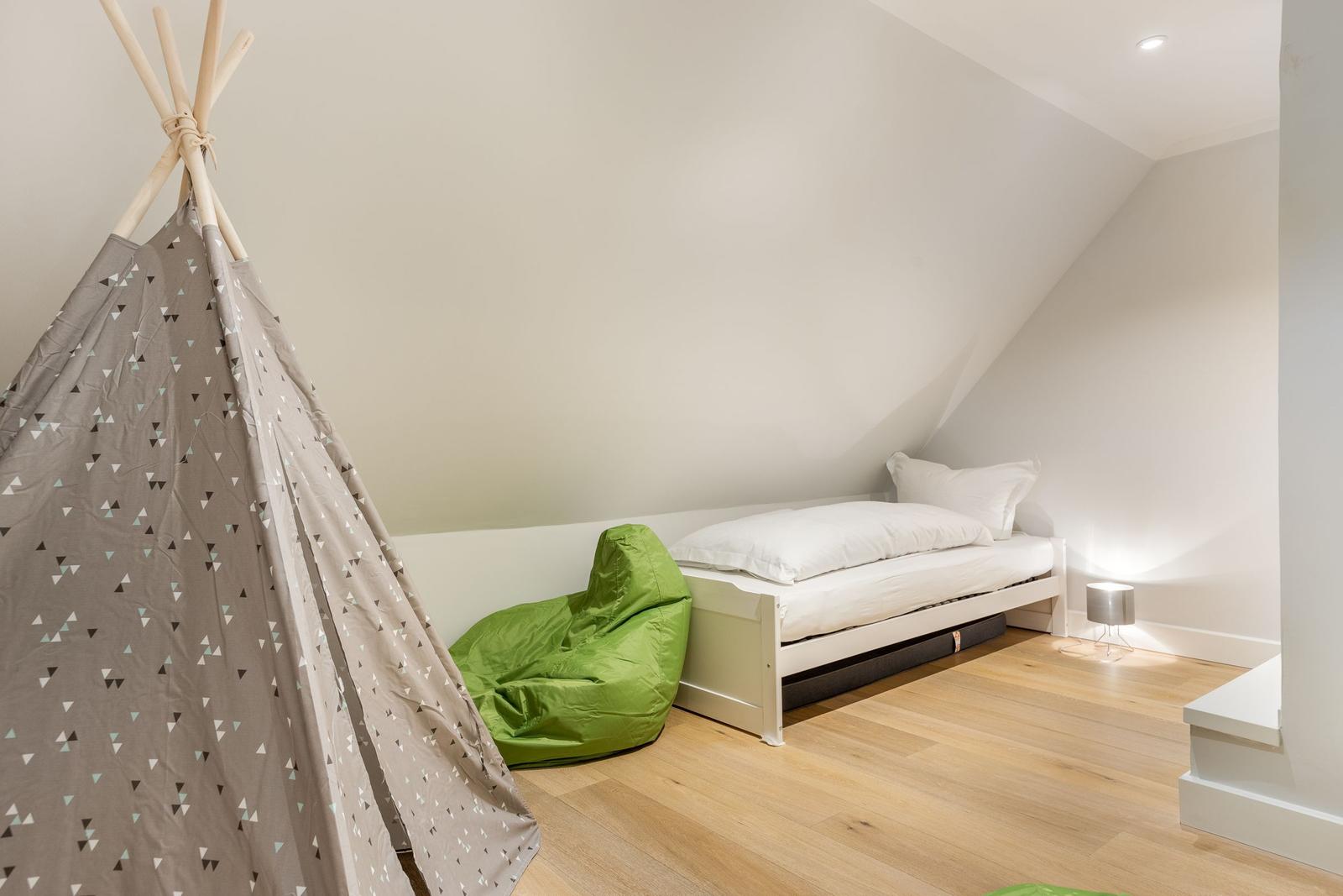 Bedroom with sloped ceiling, bed, green bean bag, and teepee.