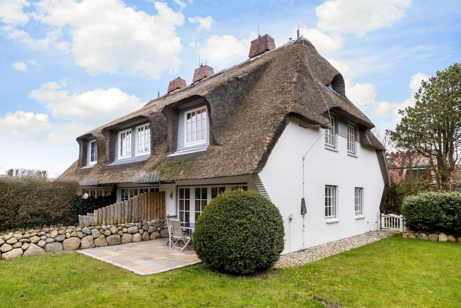 A white house with a thatched roof and terrace in the garden.