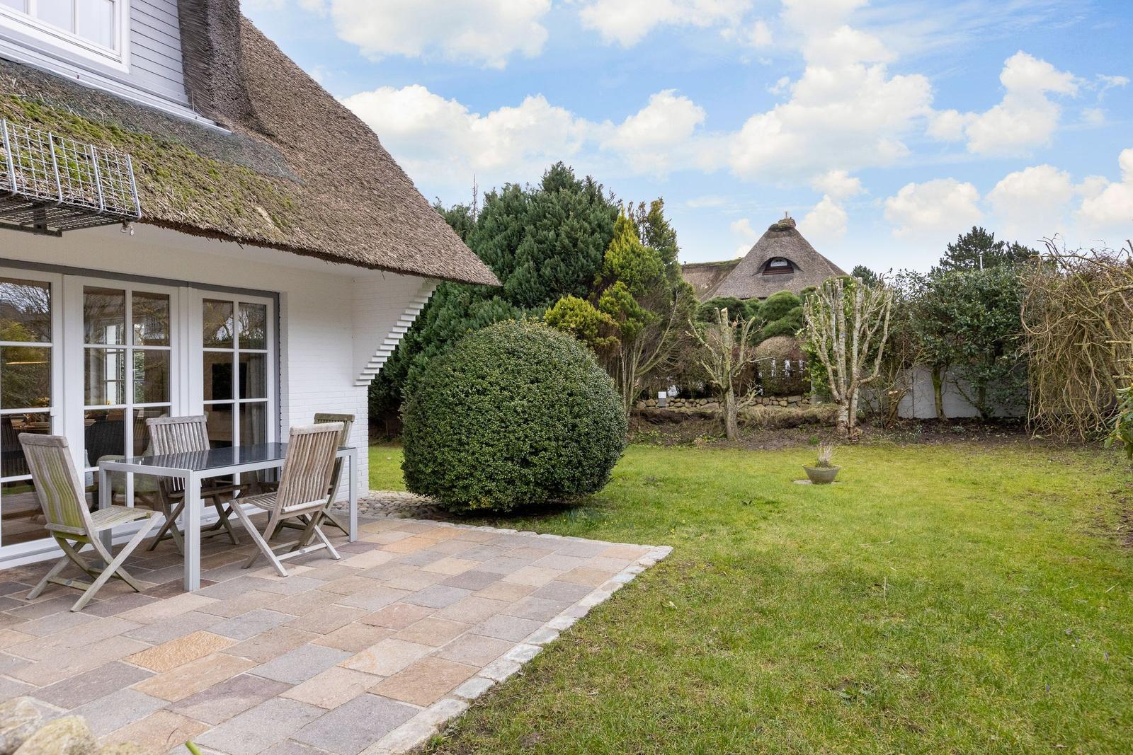 House with thatched roof, terrace, and garden. Additional buildings visible in background.