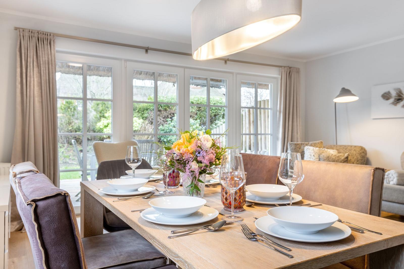 Dining table with chairs and floral decoration by windows.