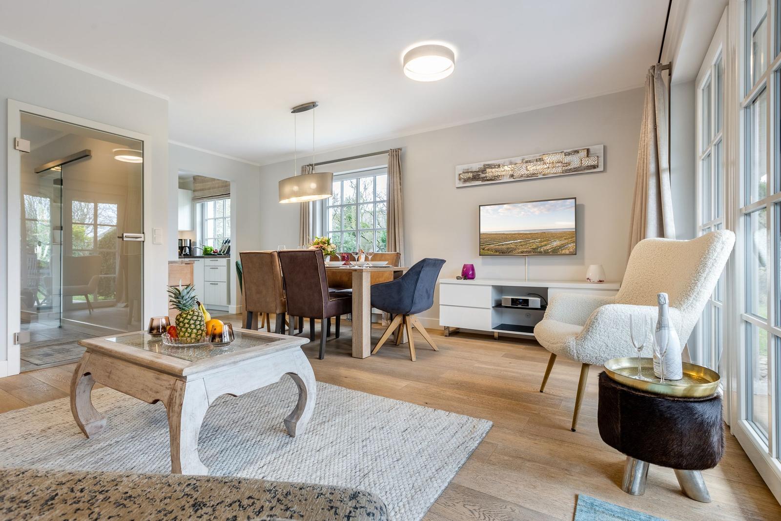 Living and dining area with wooden floor, TV, seating, and large windows.