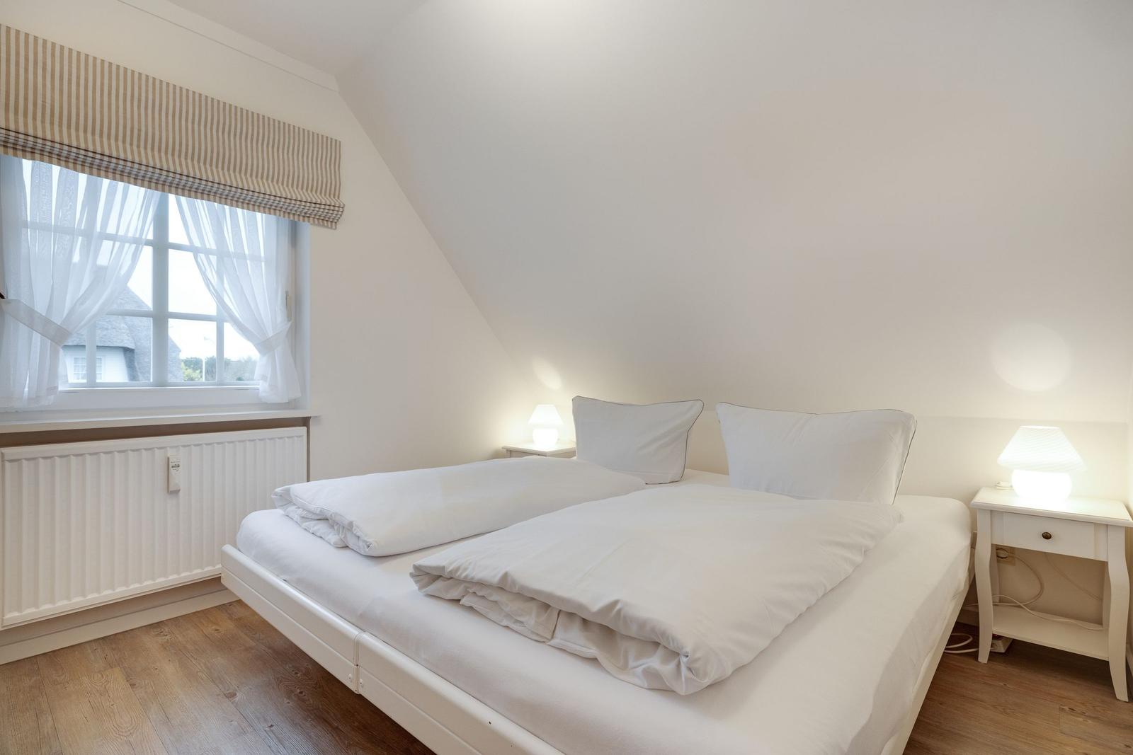 Schlafzimmer mit Doppelbett, zwei Nachttischen und Fenster mit Rollladen.