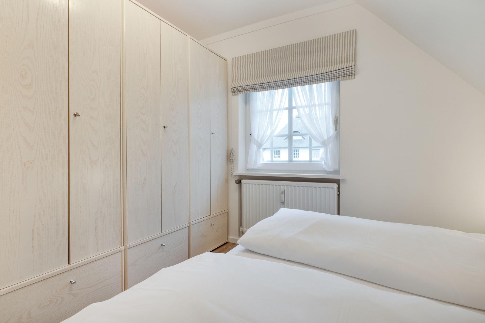 Schlafzimmer mit Bett, Kleiderschrank und Fenster mit Rollladen.