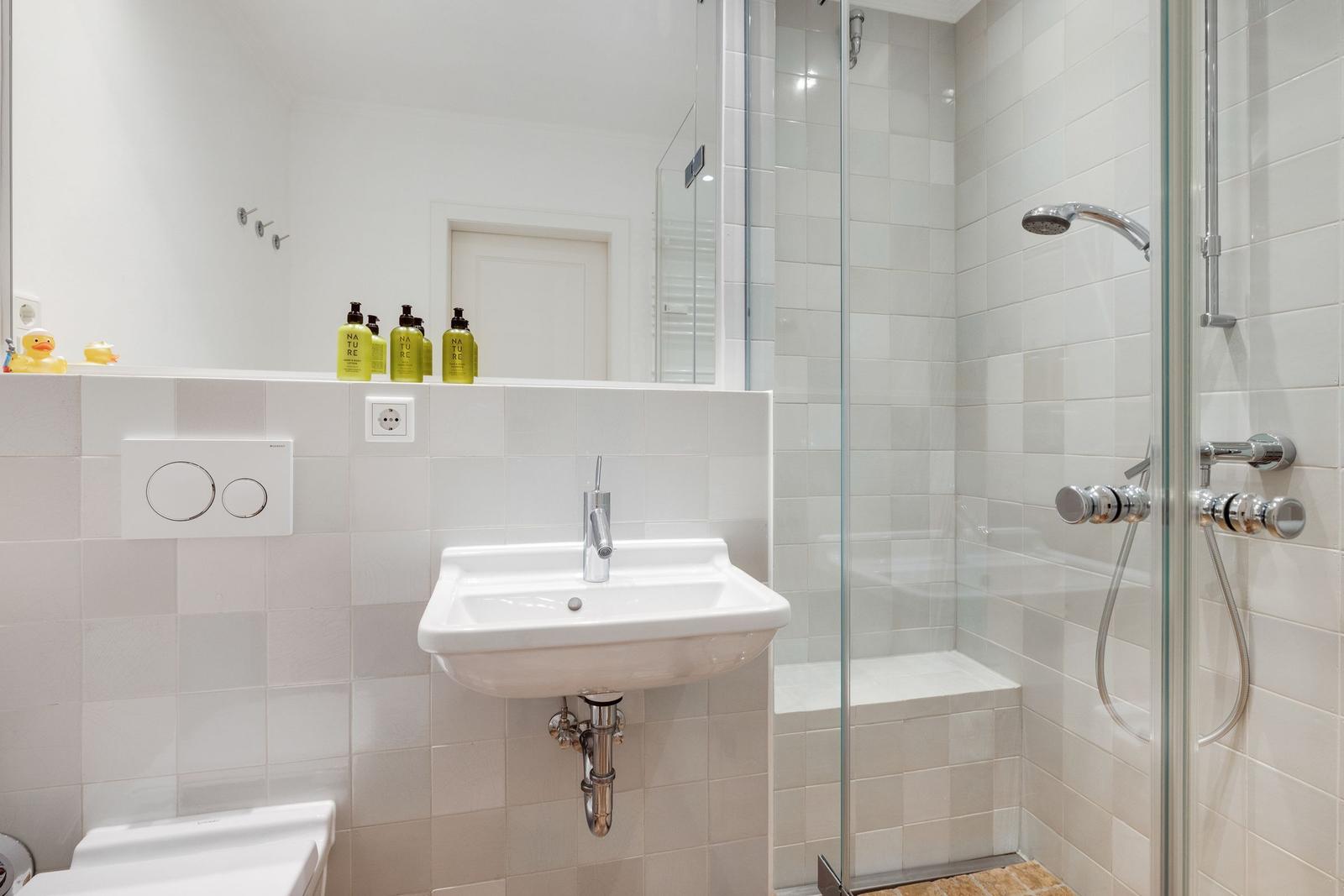 Badezimmer mit Dusche, Waschbecken und Toilette. Fliesenwand und Spiegel.