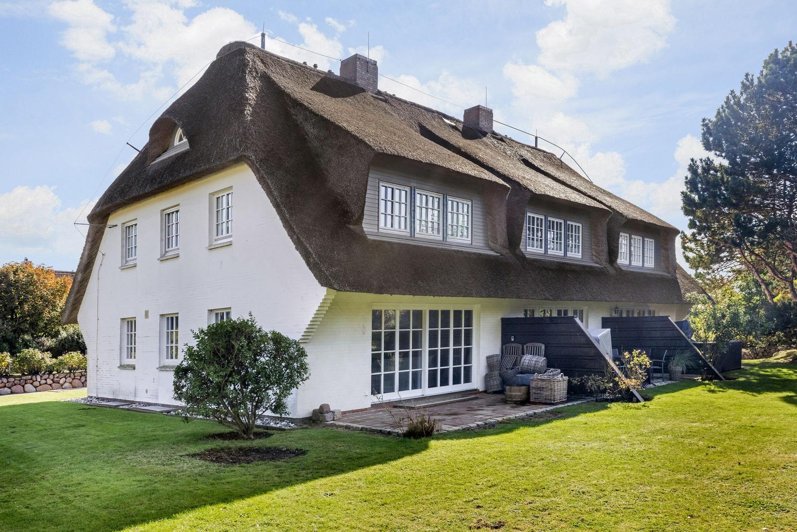 Haus mit strohgedecktem Dach, weißer Fassade und großem Garten.