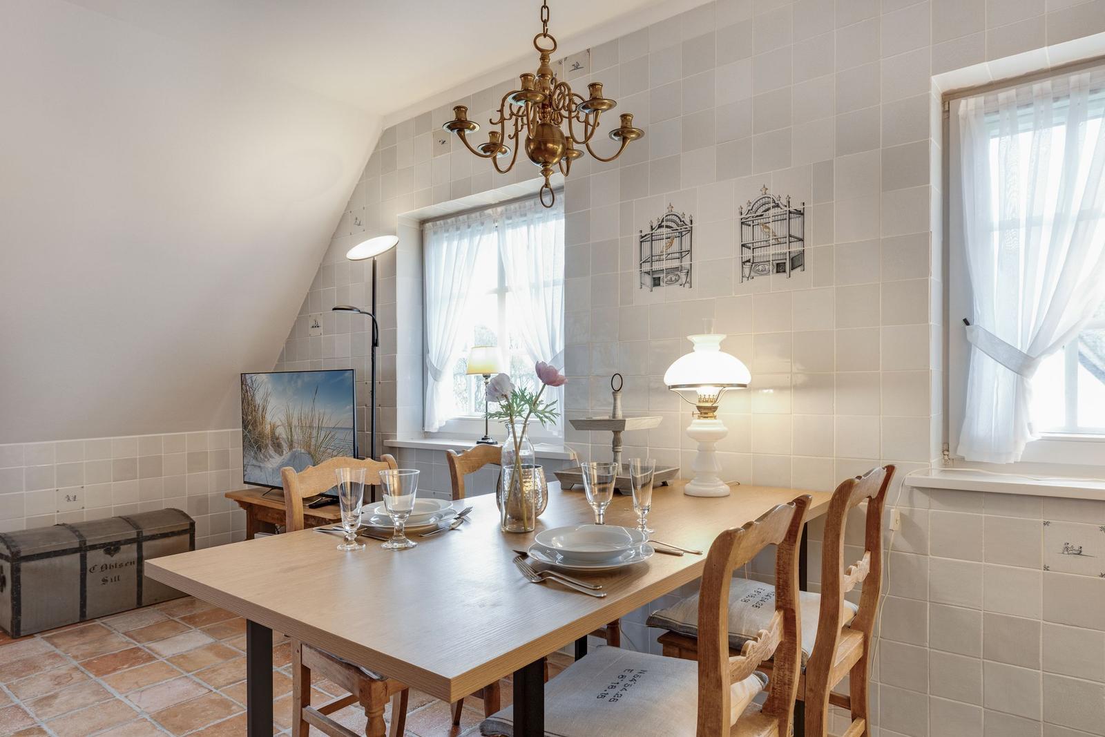 Esszimmer mit Holztisch, Stühlen und Fenstern mit weißen Vorhängen.