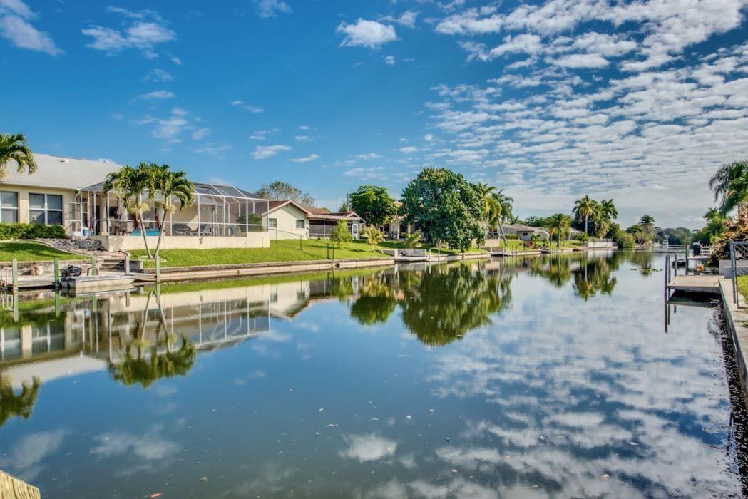 Haus am Kanal mit Palmen und Reflexionen im Wasser unter blauem Himmel.