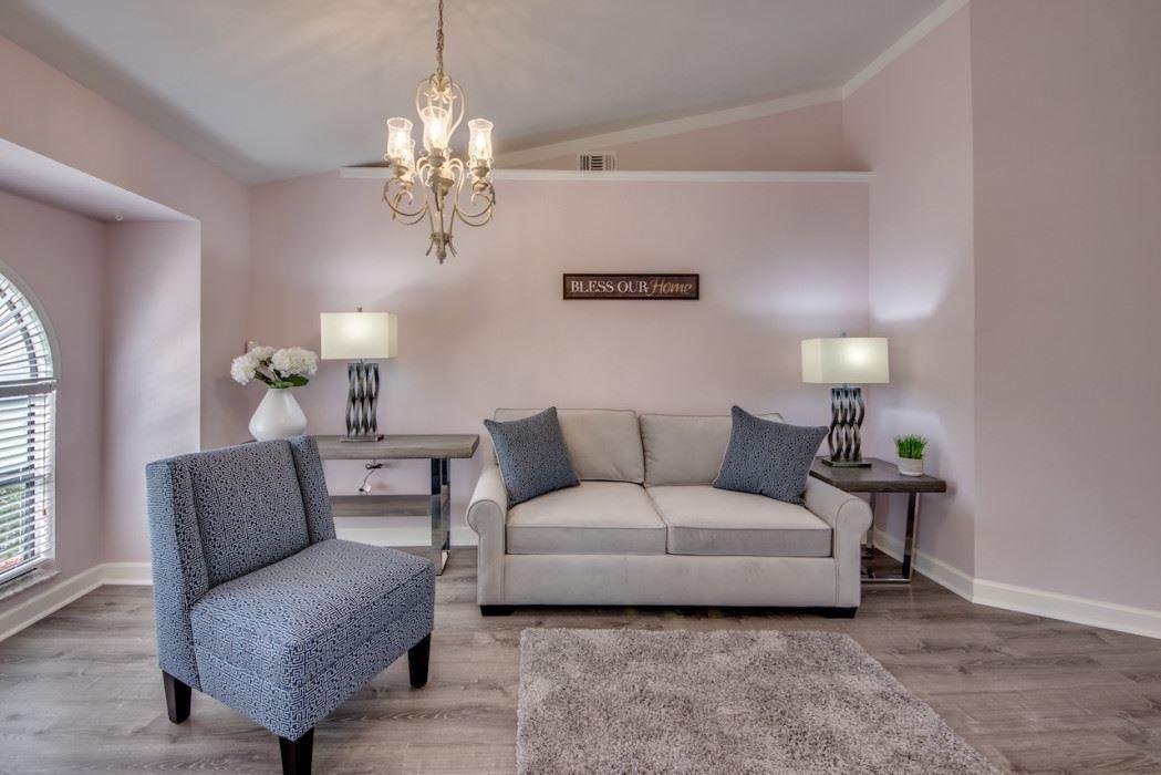 Wohnzimmer mit Sofa, Sessel, Beistelltischen und Kronleuchter an der Decke.