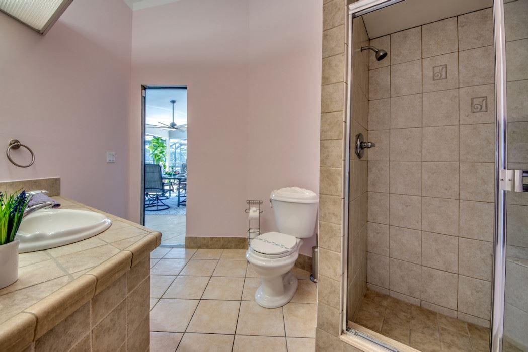 Badezimmer mit Dusche, Toilette und Waschbecken. Durchgang zu Terrasse mit Gartenmöbeln.