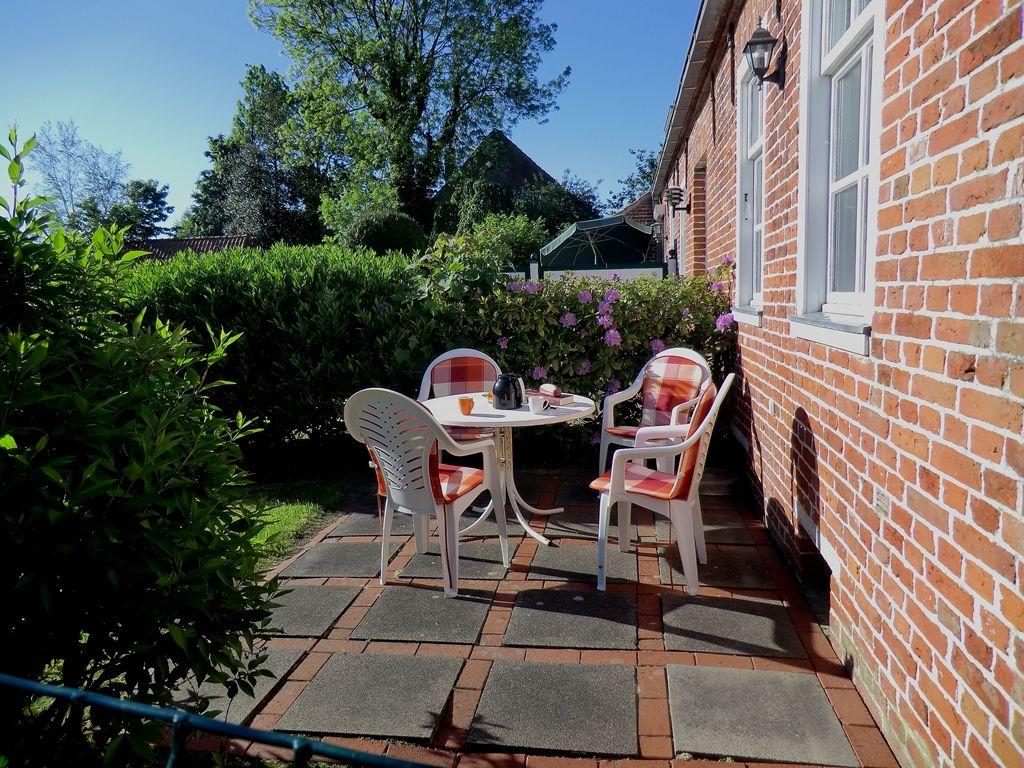 Terrasse mit Tisch und Stühlen neben rotem Backsteinhaus mit grüner Hecke.