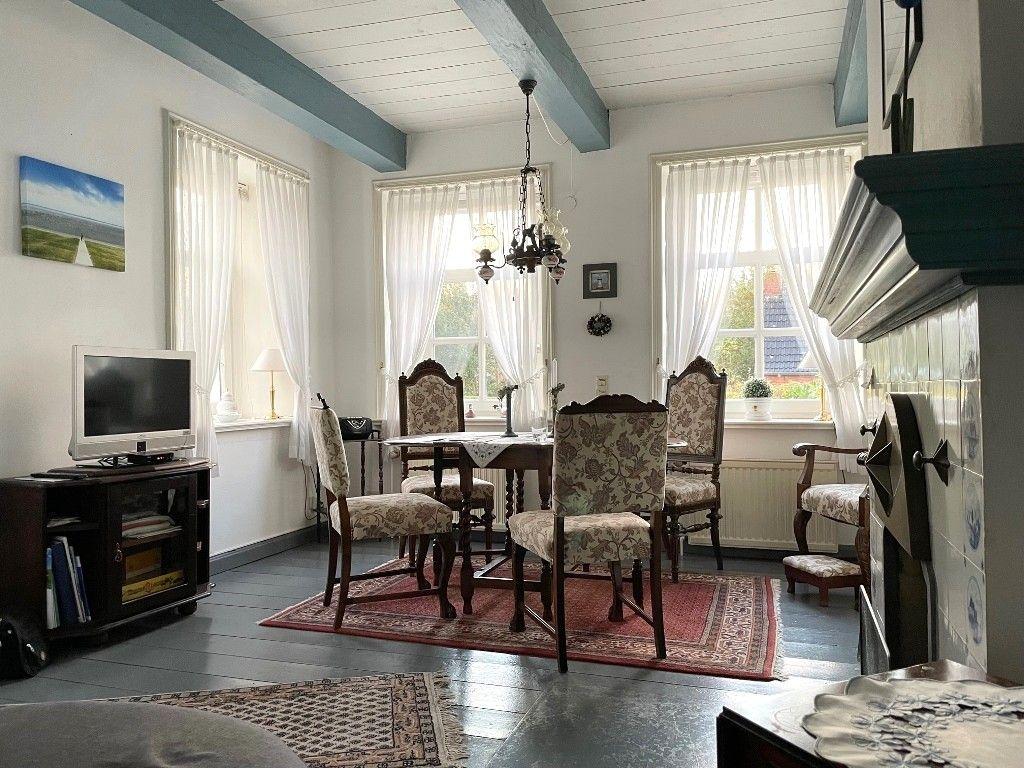 Ein Esszimmer mit Holztisch, Stühlen und Fenstern mit weißen Vorhängen.