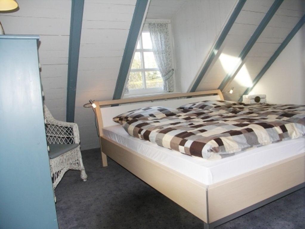 Schlafzimmer mit Dachschrägen, Bett mit gemustertem Bettzeug und Fenster mit Vorhang.
