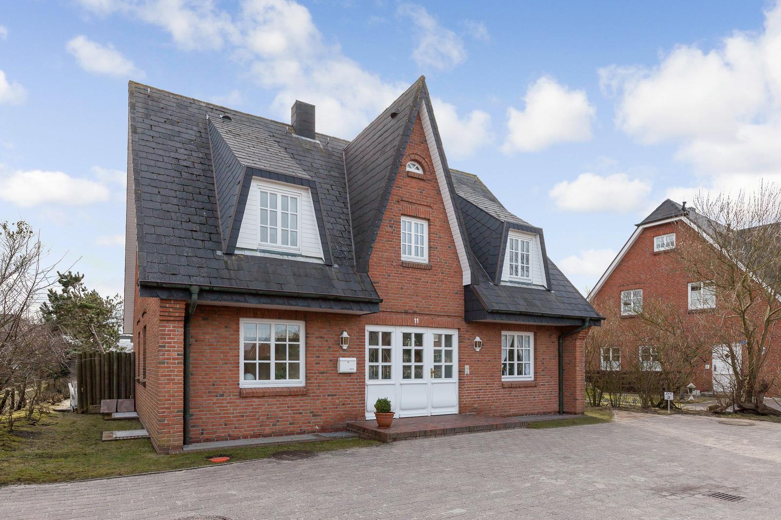 Red brick house with white windows and dark roof under blue sky.