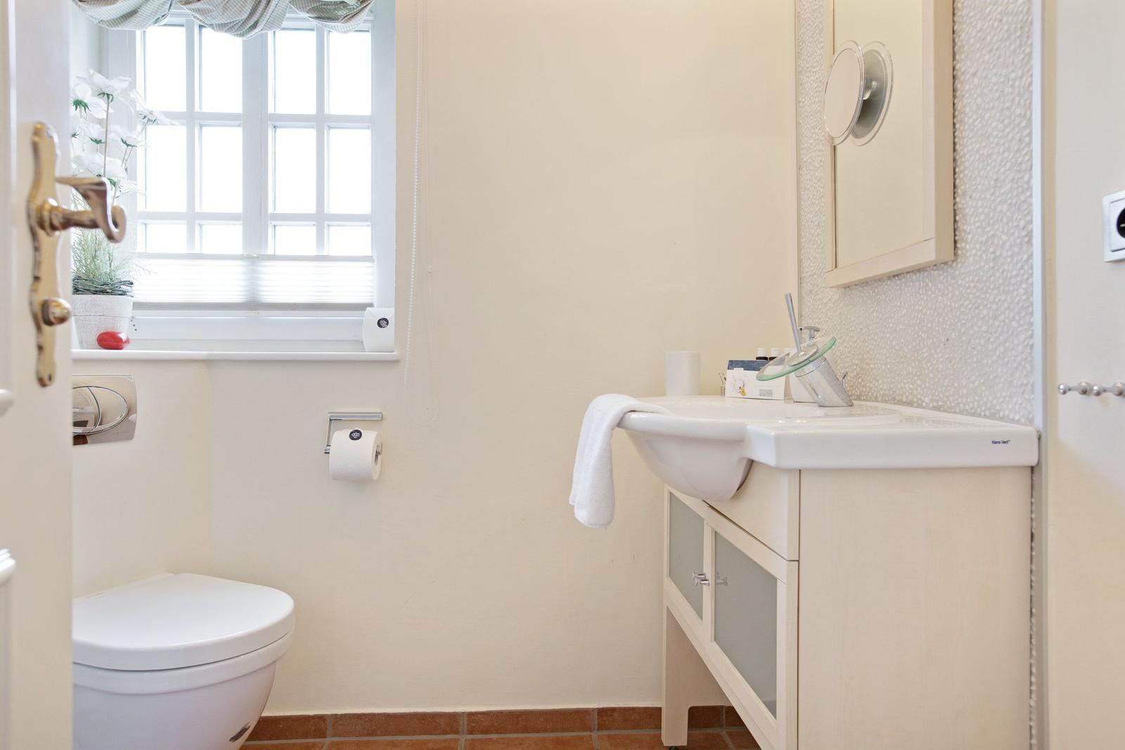 Bathroom with sink, mirror, toilet, and window.
