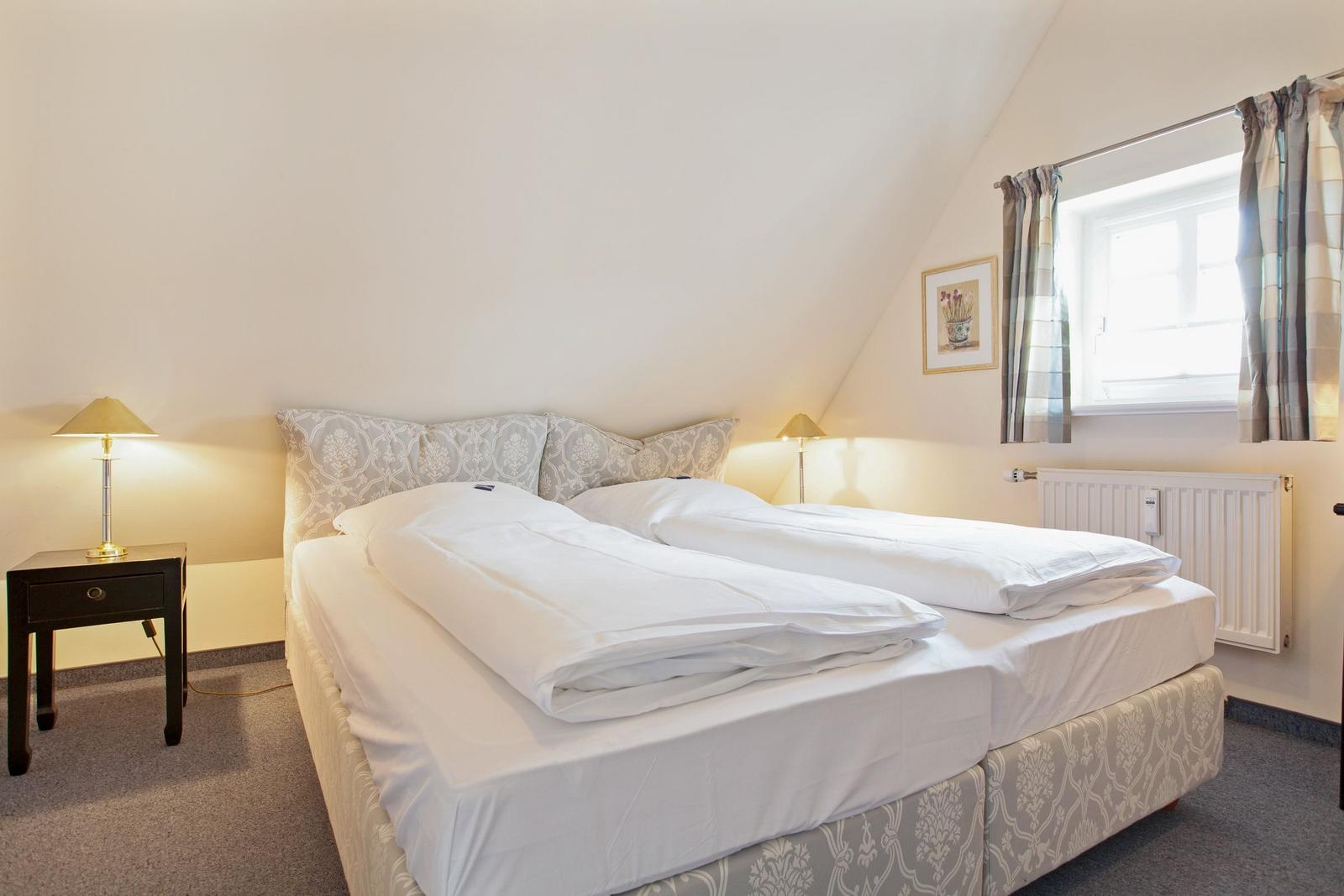 Bedroom with double bed, nightstand, and window with curtains.